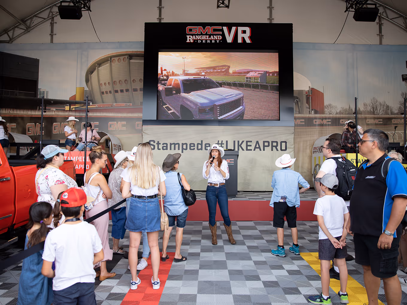 Visitors gather inside the GMC VR tent as a host presents in front of a large racing screen.