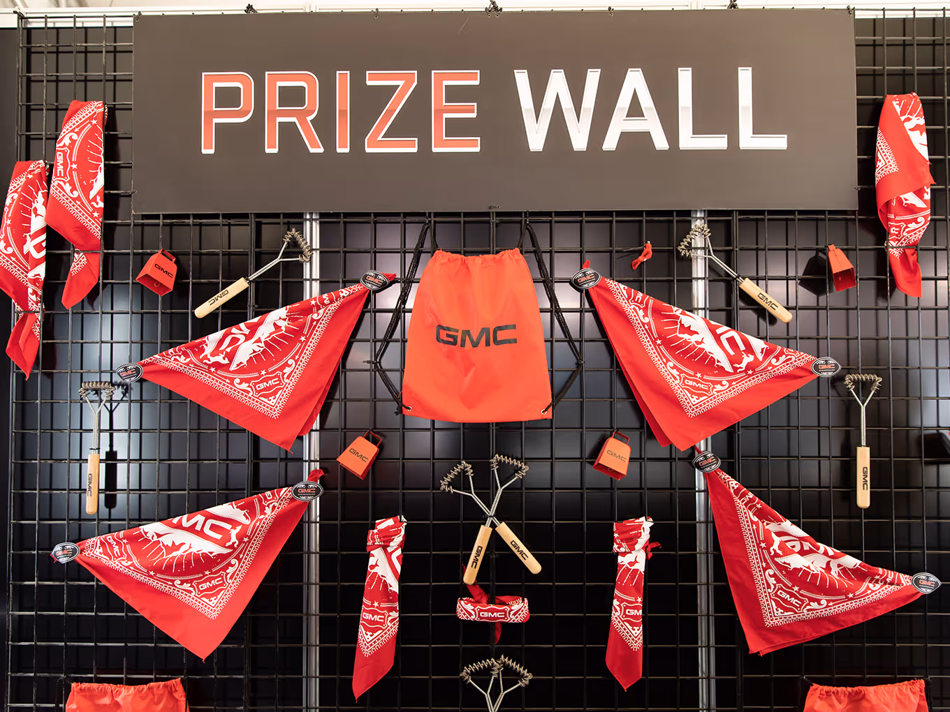 GMC prize wall featuring red bandanas, swag items, and branded giveaways on a black grid display.