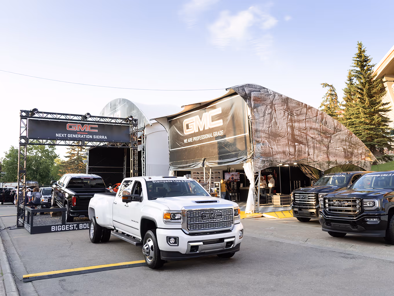 Lineup of GMC trucks parked beside the VR activation tent branded “We Are Professional Grade.”