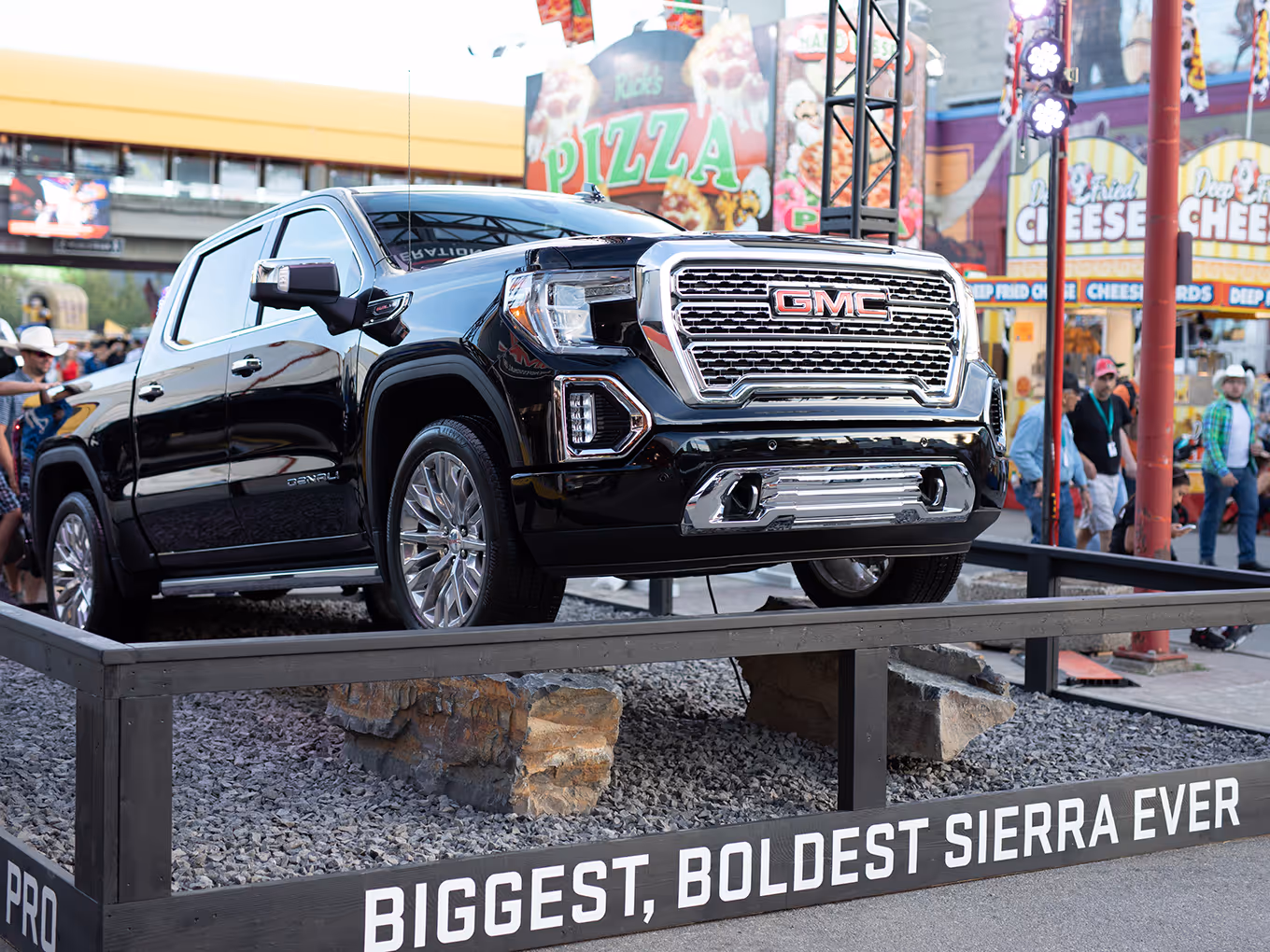 Black GMC Sierra showcased on raised rock platform surrounded by Calgary Stampede midway attractions.