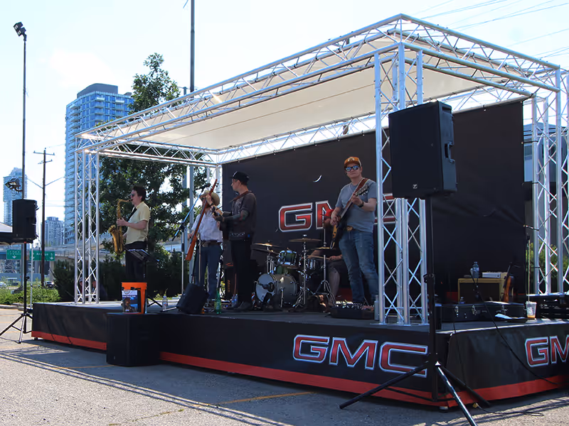 Live music performance on a GMC-branded stage with truss structure at a Calgary Stampede pop-up event.