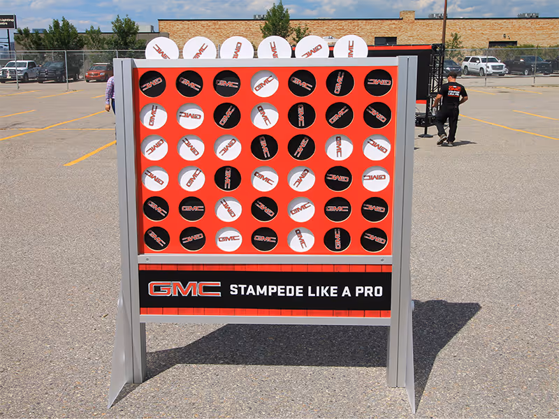 Oversized Connect Four game with custom GMC “Stampede Like a Pro” branding at a dealership event.