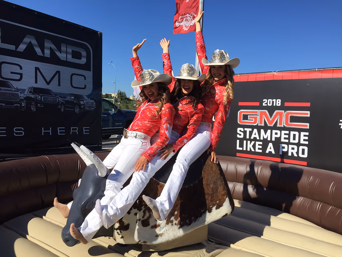 Three Stampede performers pose on the mechanical bull at a GMC community pop-up.