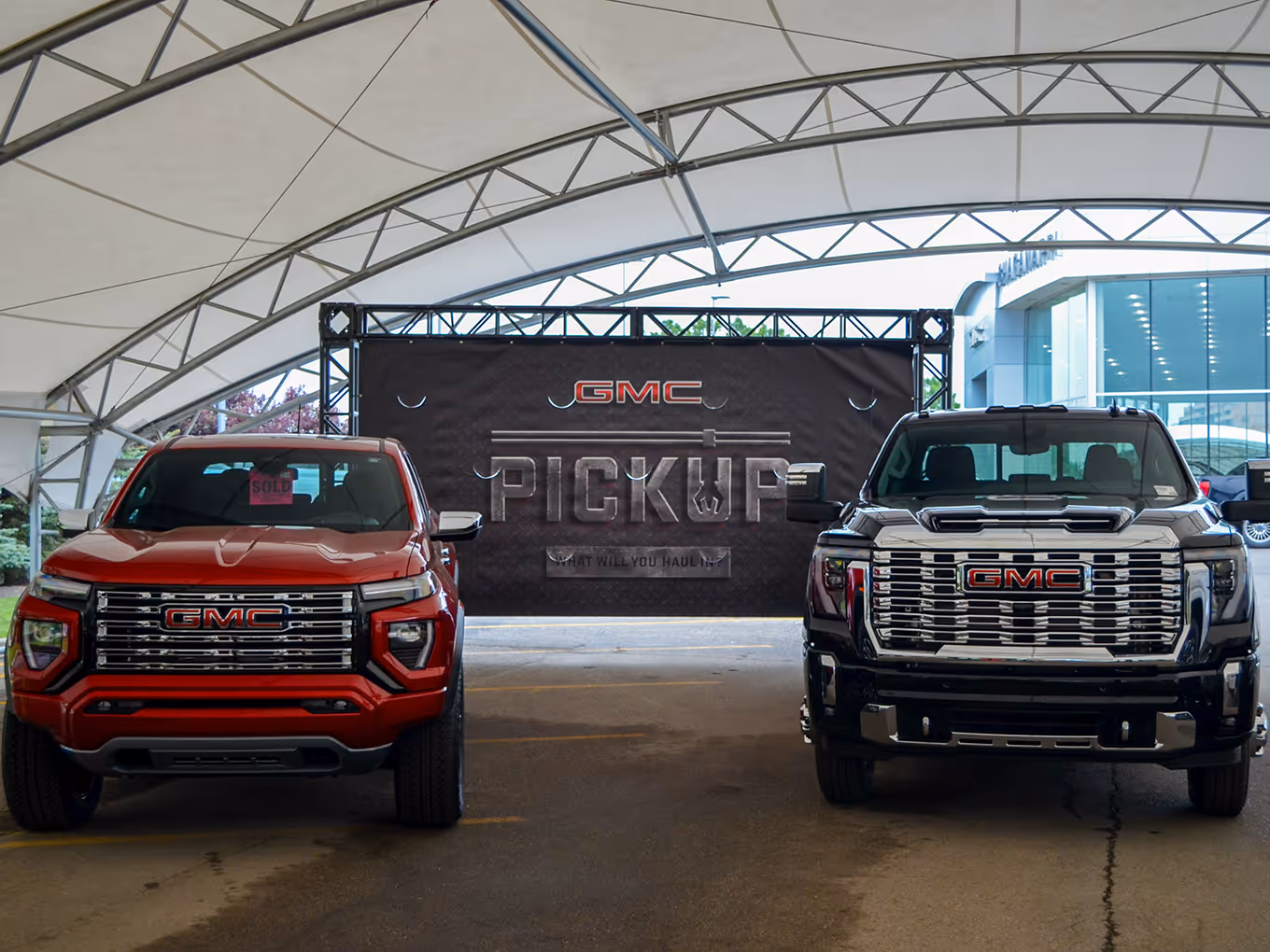Red and black GMC trucks displayed under a branded “Pickup” rental truss backdrop at a Stampede event.
