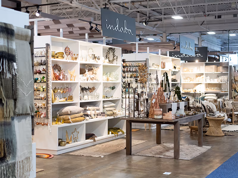 Freestanding white shelving units filled with home décor products in the Indaba custom booth framed by pergola-style accents.