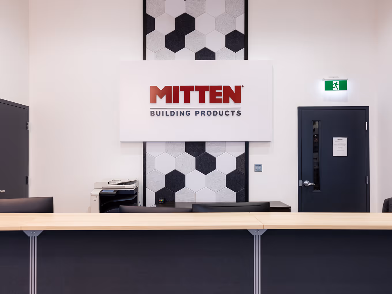 custom-built Reception area with Mitten Building Products logo mounted over a hexagon acoustic felt feature wall.