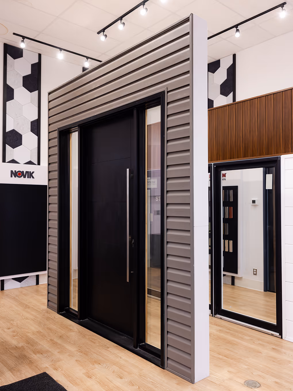 Full-size exterior door display featuring a modern black door framed by gray siding panels inside the Mitten showroom.