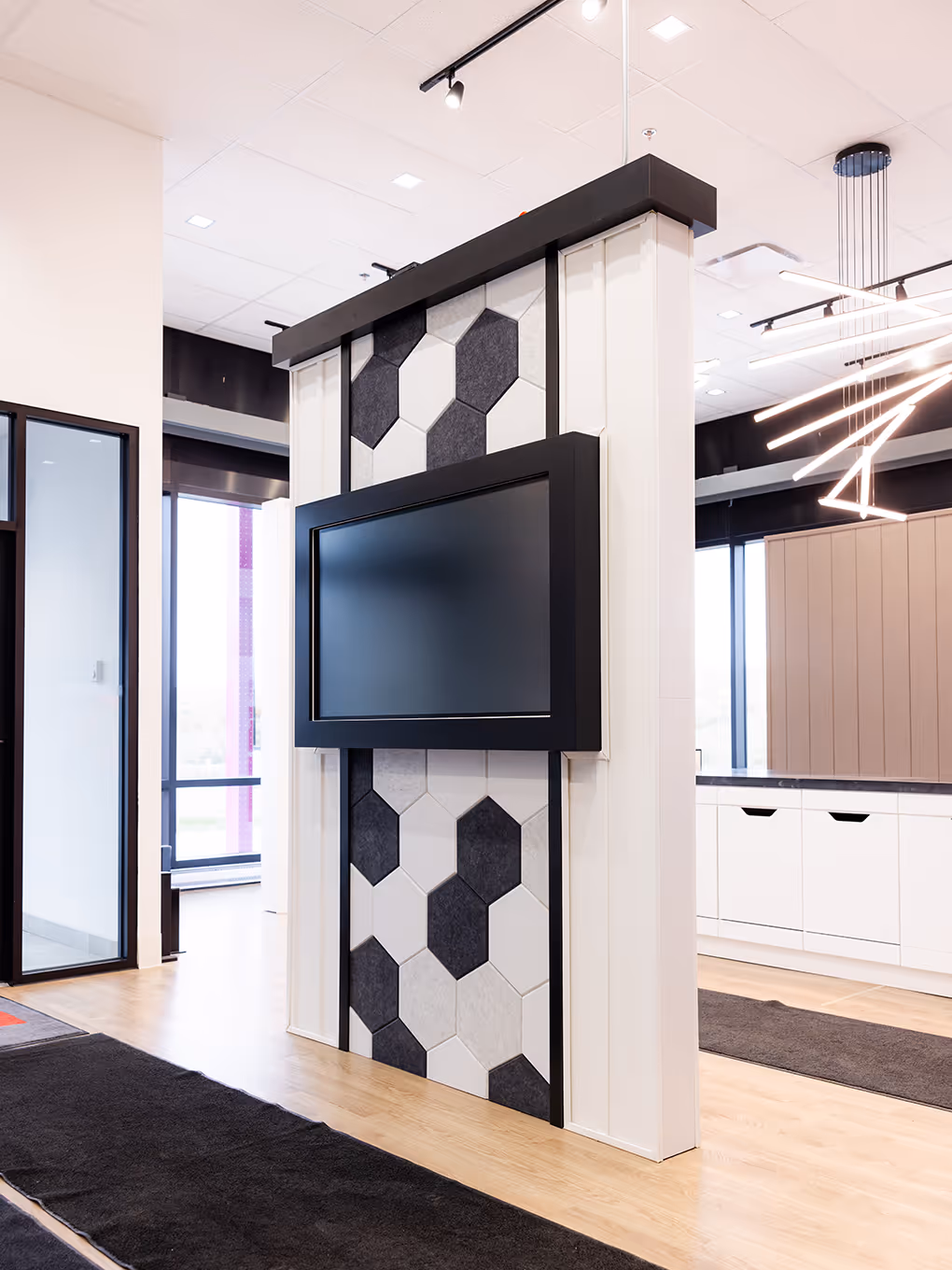 Showroom feature wall with a large screen surrounded by hexagon acoustic felt tiles in black, white, and gray.