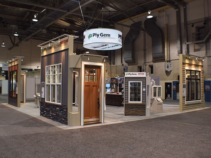 Corner angle of the Ply Gem and Mitten island exhibit showing multiple window and siding displays arranged in an open-concept trade show layout.