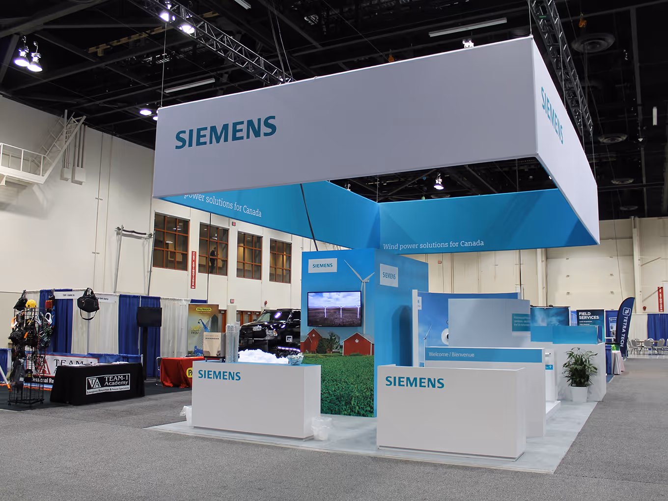 Wide view of Siemens modular exhibit with custom reception counters, Pantone-matched blue plexi-style walls, and suspended overhead signage at the Calgary BMO Centre.