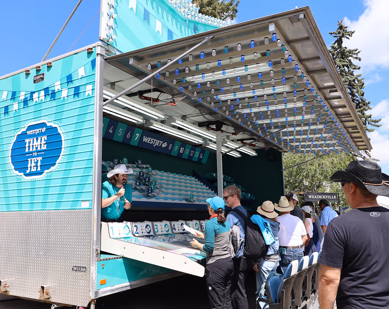 Front view of WestJet’s “Time to Jet” midway game with crowds playing the custom airplane-racing lanes inside the refurbished carnival trailer.