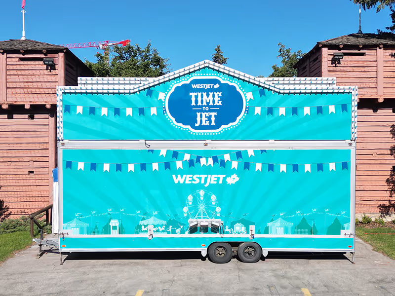 Front-facing image of the WestJet “Time to Jet” carnival trailer with refreshed teal graphics for the Calgary Stampede midway.
