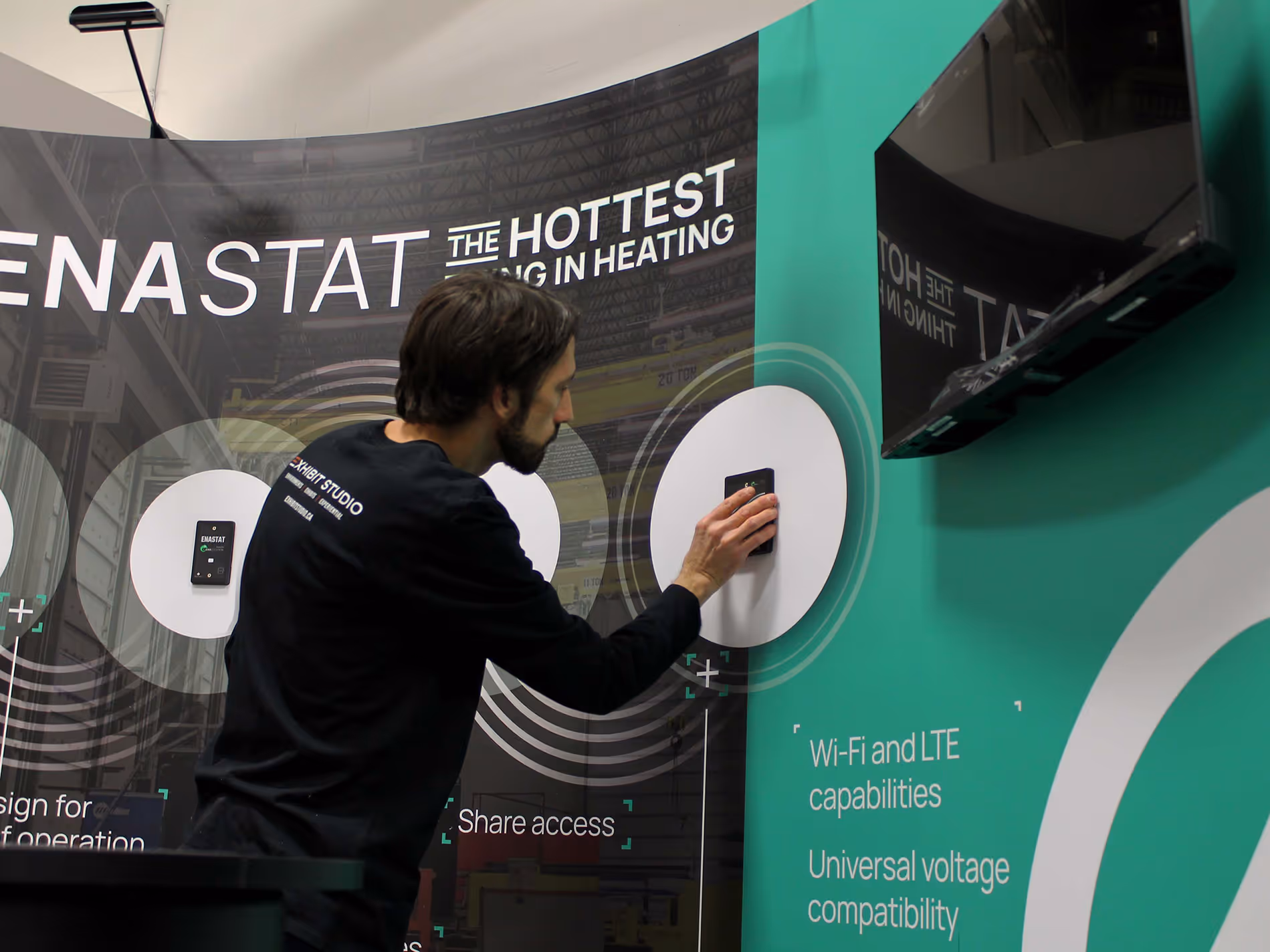 Exhibit Studio technician installing ENA Solutions smart thermostat onto CNC-cut aluminum mounting panel for interactive trade show display functionality.