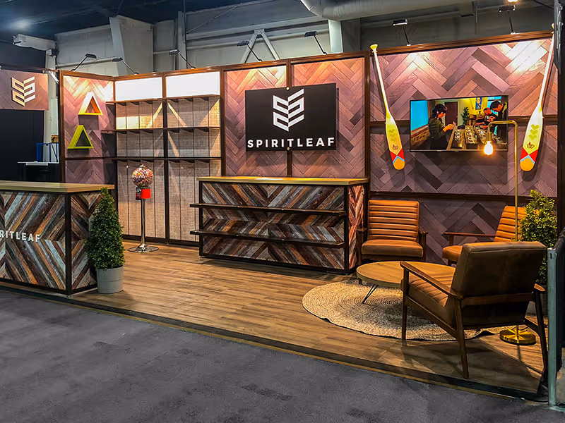 Spiritleaf modular 10x20 trade show display showing product shelving, apparel hooks, gumball machine, and feature lighting against herringbone wood panels.