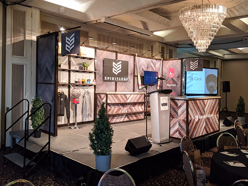 Spiritleaf AGM backdrop display featuring retail-style product wall, branded signage, podium, and decorative greenery on a raised stage.