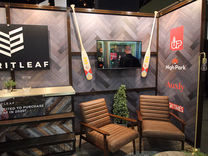 Spiritleaf lounge corner in modular exhibit with branded wall graphics, lounge chairs, greenery, and a wall-mounted video display.