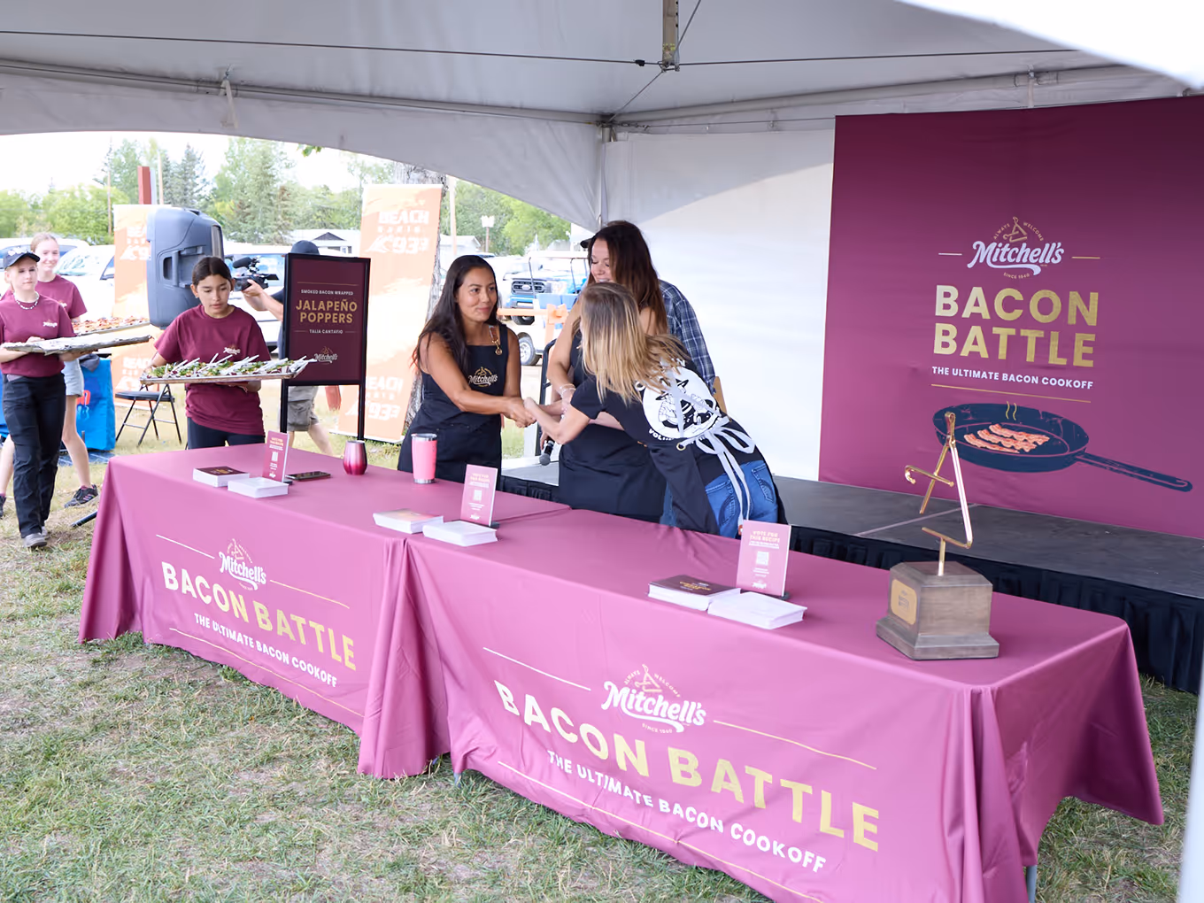 Mitchell’s Bacon Battle event setup featuring branded flags, fabric table covers, and competitors preparing dishes for the live cook-off.