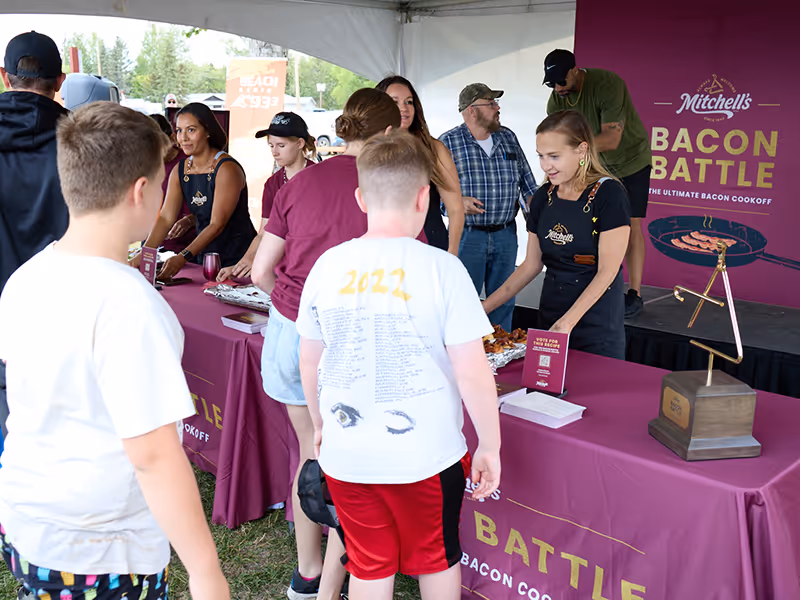 Branded Mitchell’s Bacon Battle outdoor booth with custom tablecloths and signage at Cochin Days live cook-off event.