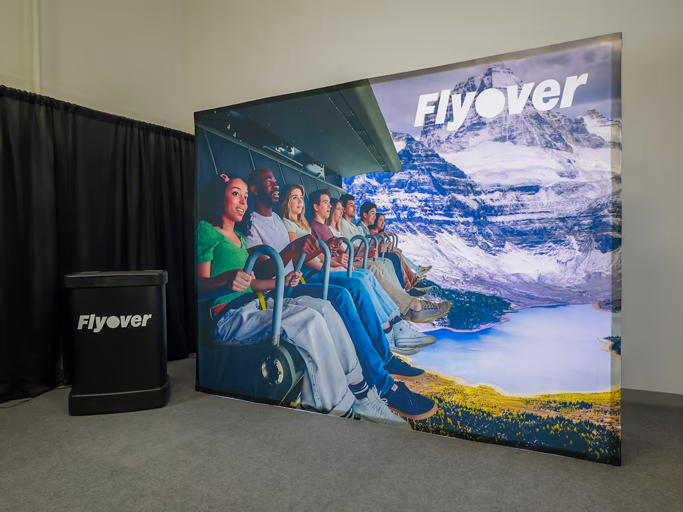 Backlit FlyOver display showing guests on the ride against a mountain backdrop, with a branded counter beside it.