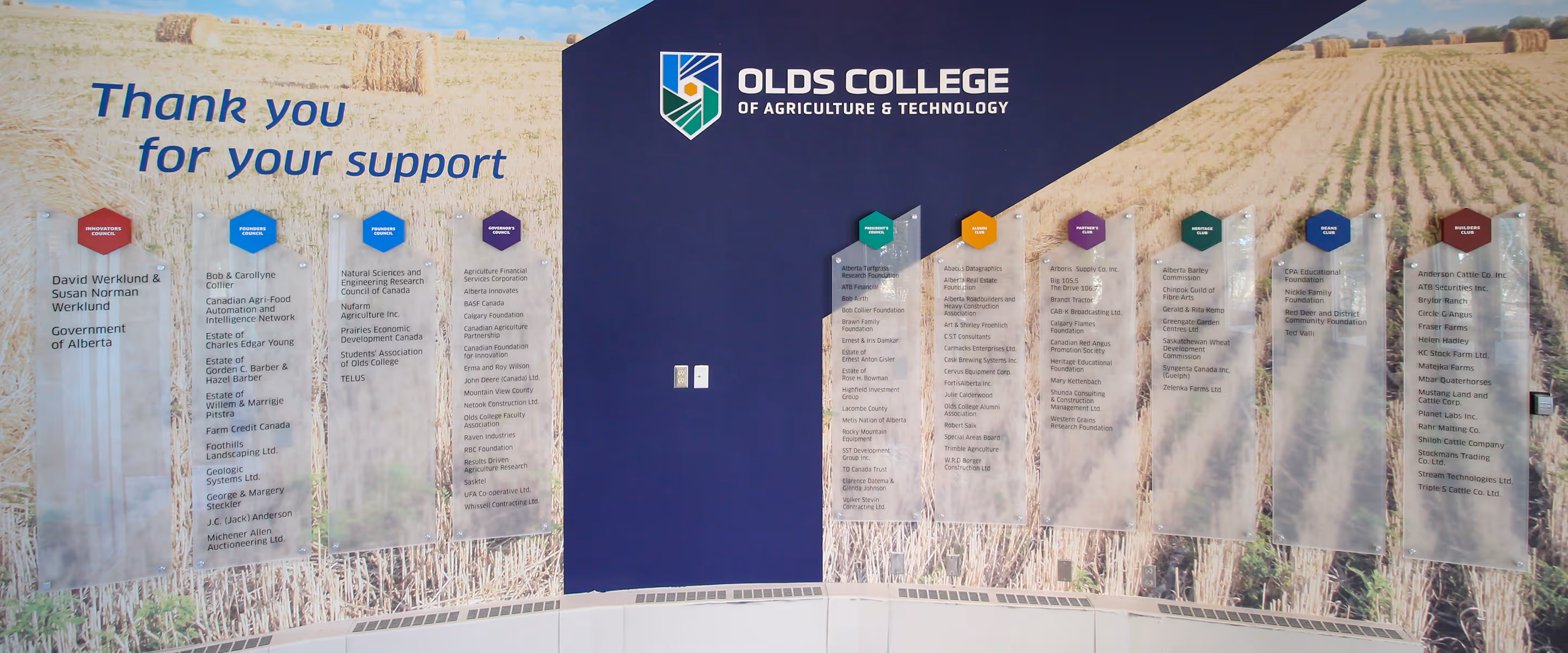 Olds College donor recognition wall with scenic vinyl graphics, frosted acrylic panels, hexagon caps, and a dimensional logo on a curved feature wall.