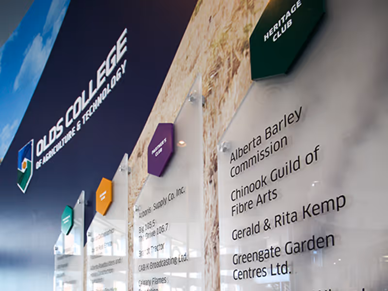 Angled view of Olds College donor plaques with frosted acrylic panels, hexagon caps, and agricultural vinyl graphics.