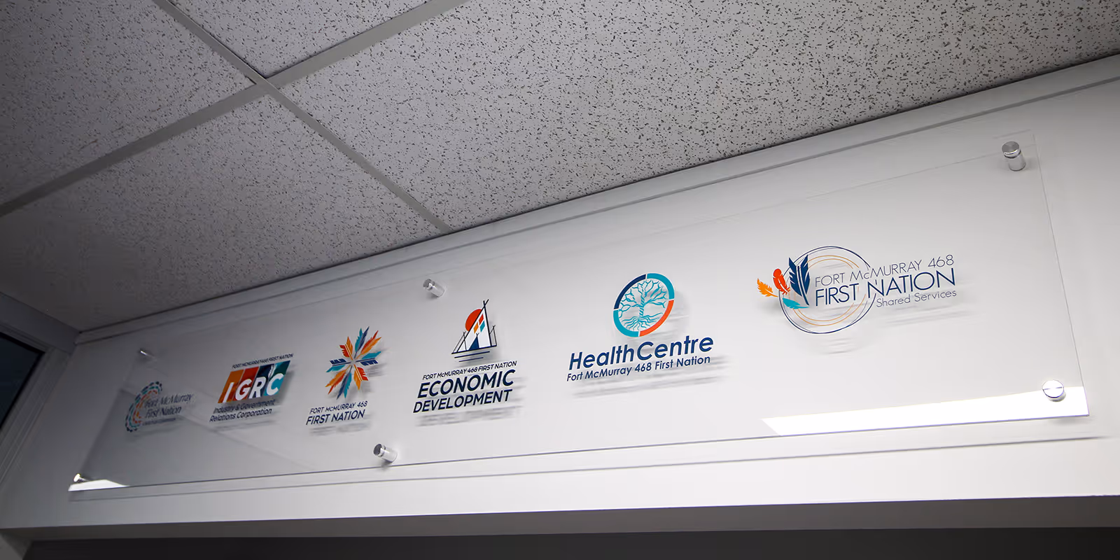Acrylic sign panel displaying Fort McMurray 468 First Nation department logos, installed with standoffs for clean interior office signage