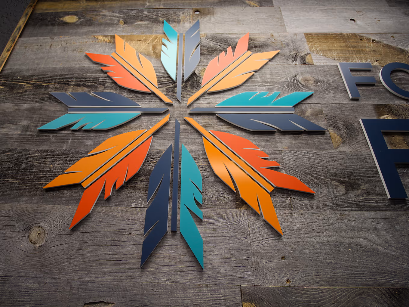 Close-up of Fort McMurray 468 First Nation 3D feather logo mounted on a textured wood feature wall for interior office branding.