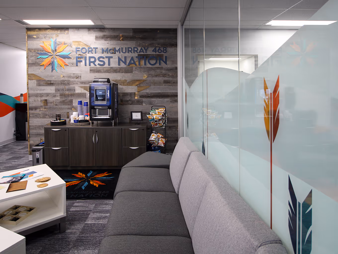 Fort McMurray 468 First Nation lounge area with wood feature wall, 3D logo, and glass privacy film with arrow graphics.