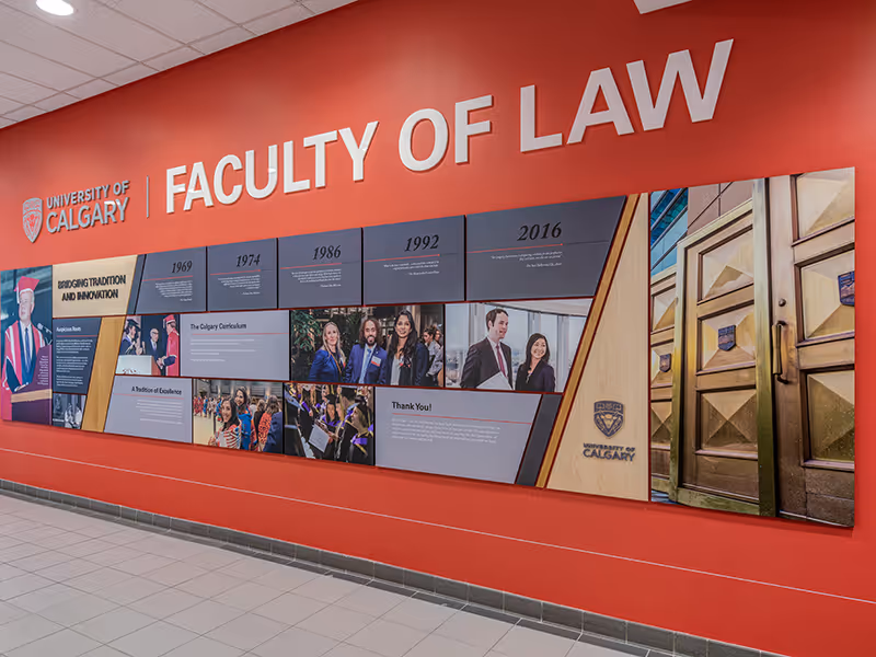 Wide view of the University of Calgary Faculty of Law history display spanning a red feature wall.