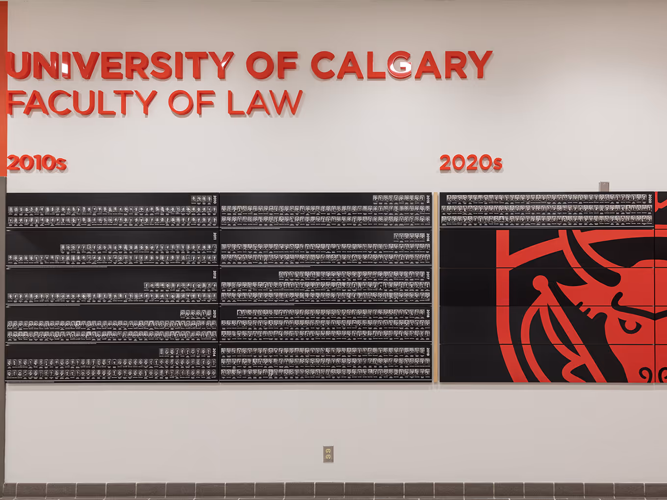University of Calgary Faculty of Law graduation recognition wall featuring graduate portraits organized by decade.