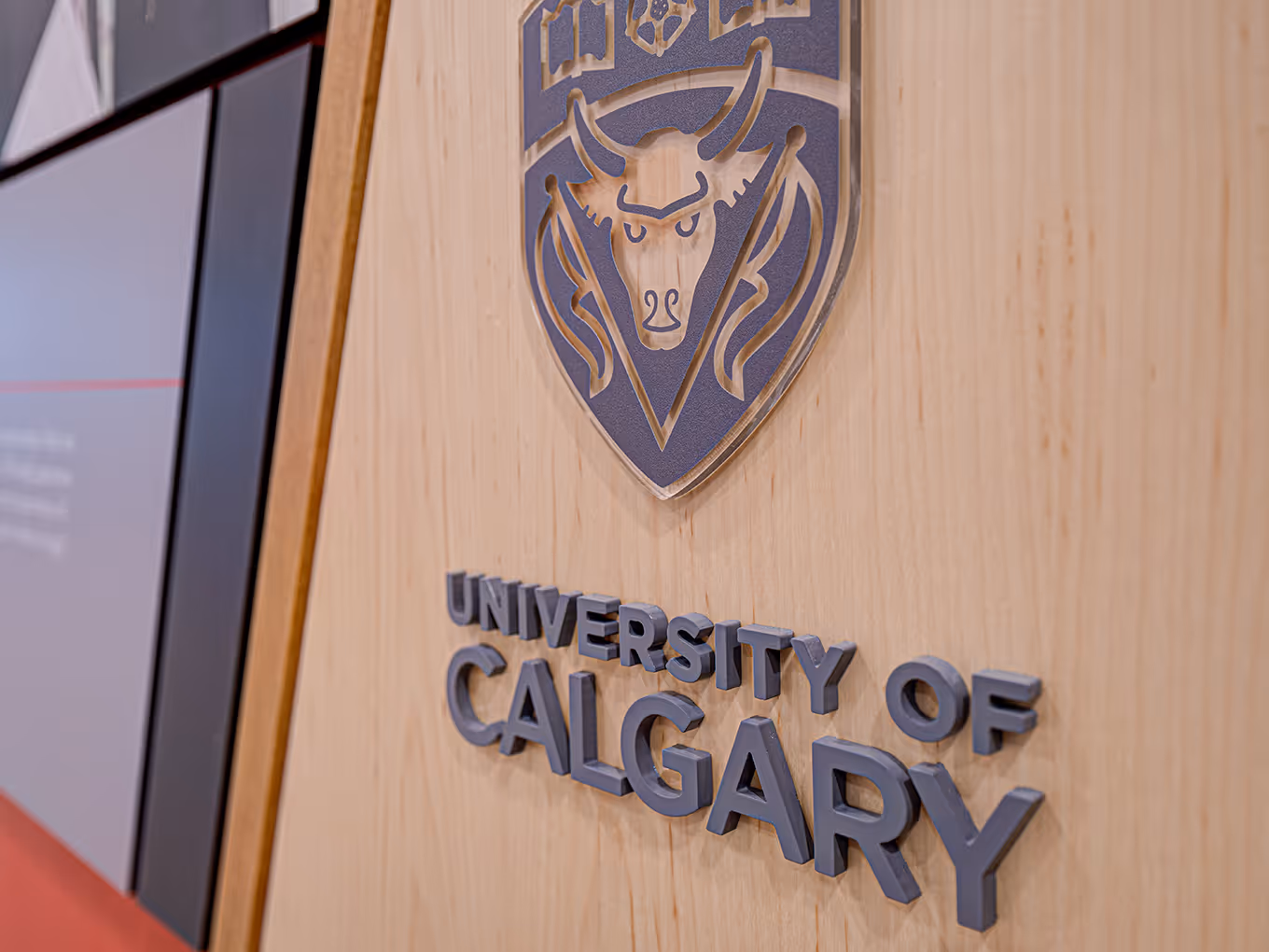 Close-up of University of Calgary crest and dimensional lettering mounted on a wood-finished panel within the Faculty of Law display.