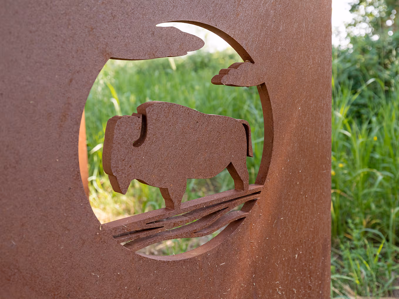 Detail of a custom-fabricated steel base featuring a cut-out bison graphic, finished with a weathered patina to blend into the natural landscape.