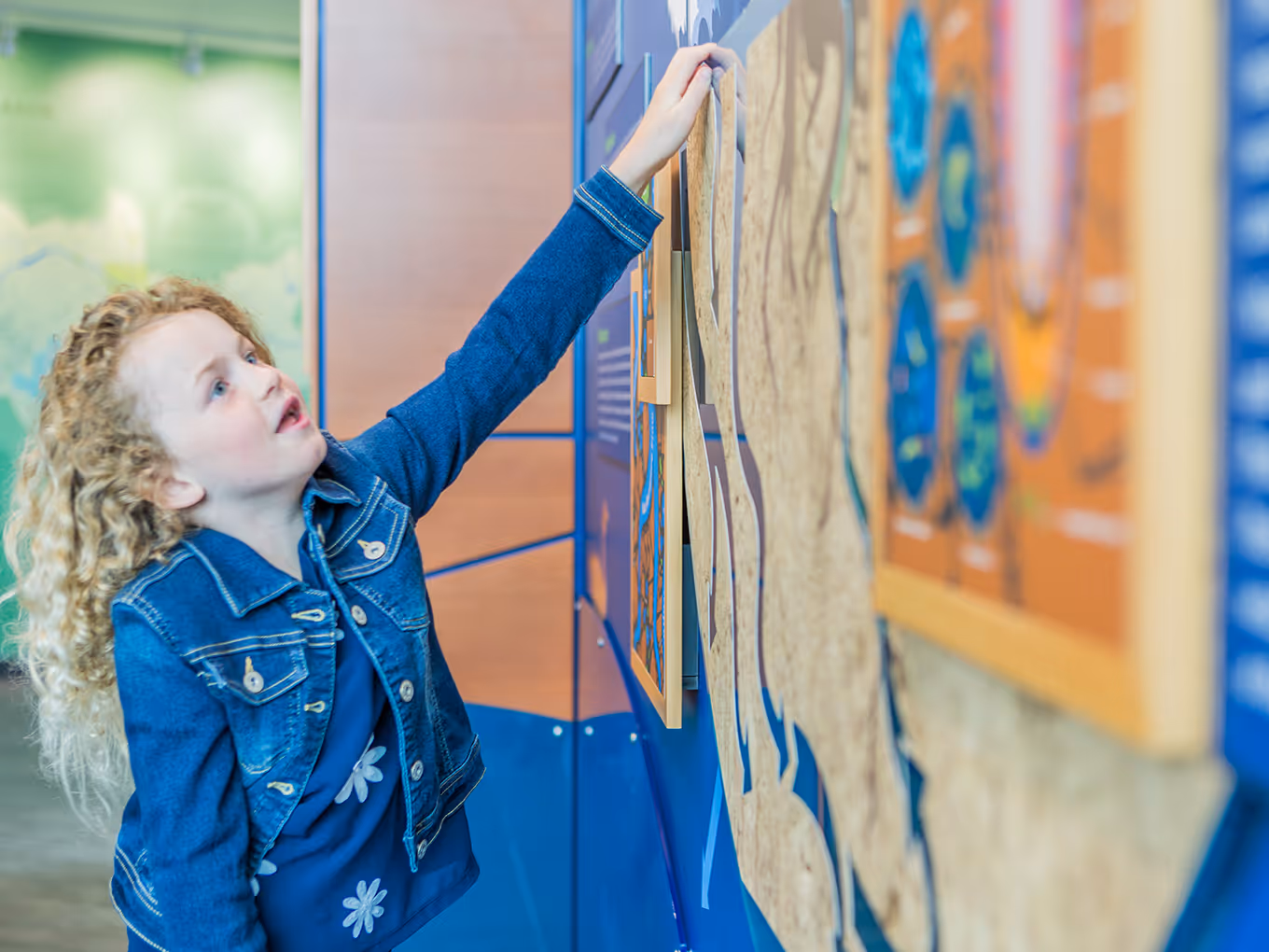Child engaging with a tactile, layered wall exhibit that explains soil, water, and environmental processes.