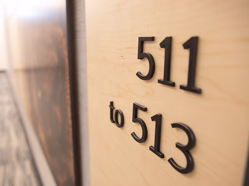 Close-up of room number signage with raised lettering on a natural wood panel.