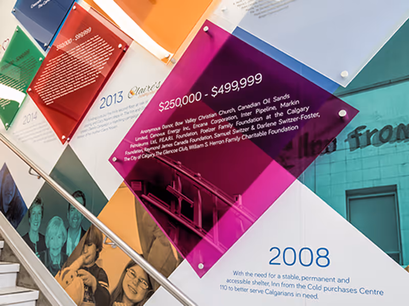 Interior wall featuring branded donor recognition signage and layered acrylic elements in Inn from the Cold facility.