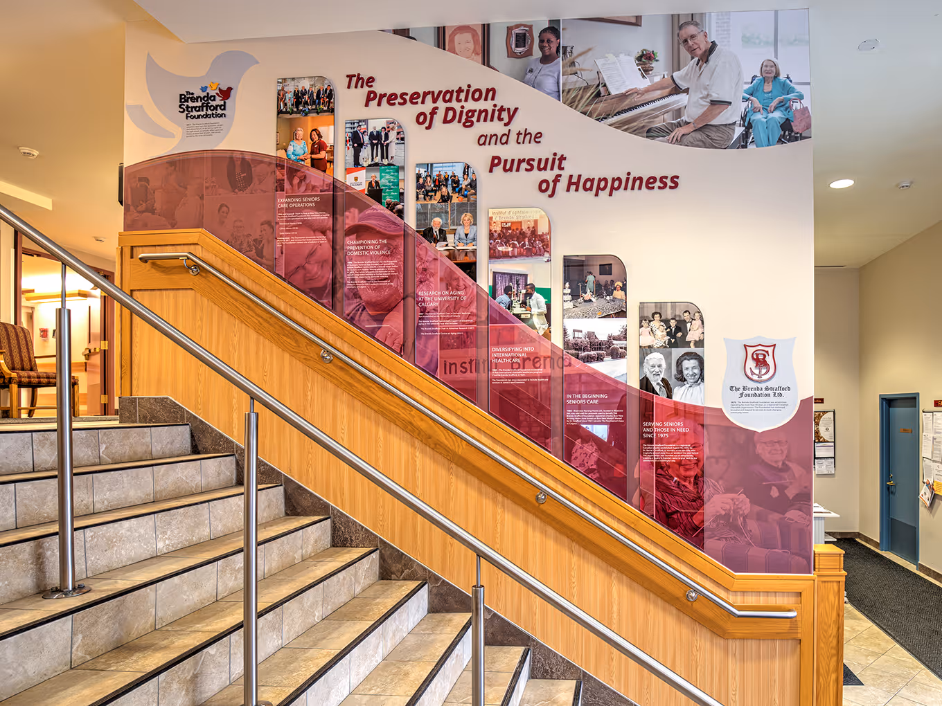 Full-height donor wall installation wrapping the stairwell at Clifton Manor with branded graphics, photos, and dimensional signage.