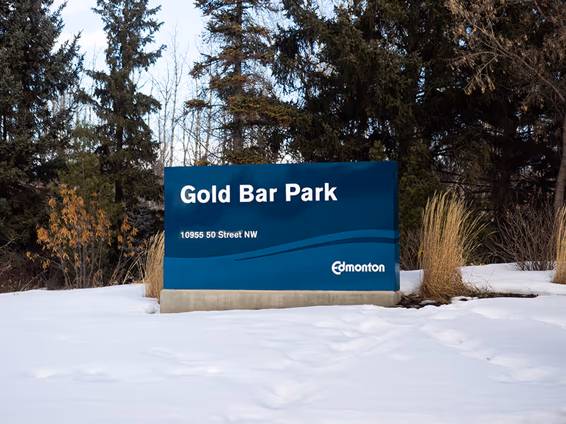 Gold Bar Park identification sign with wave graphic and Edmonton logo, surrounded by winter trees.