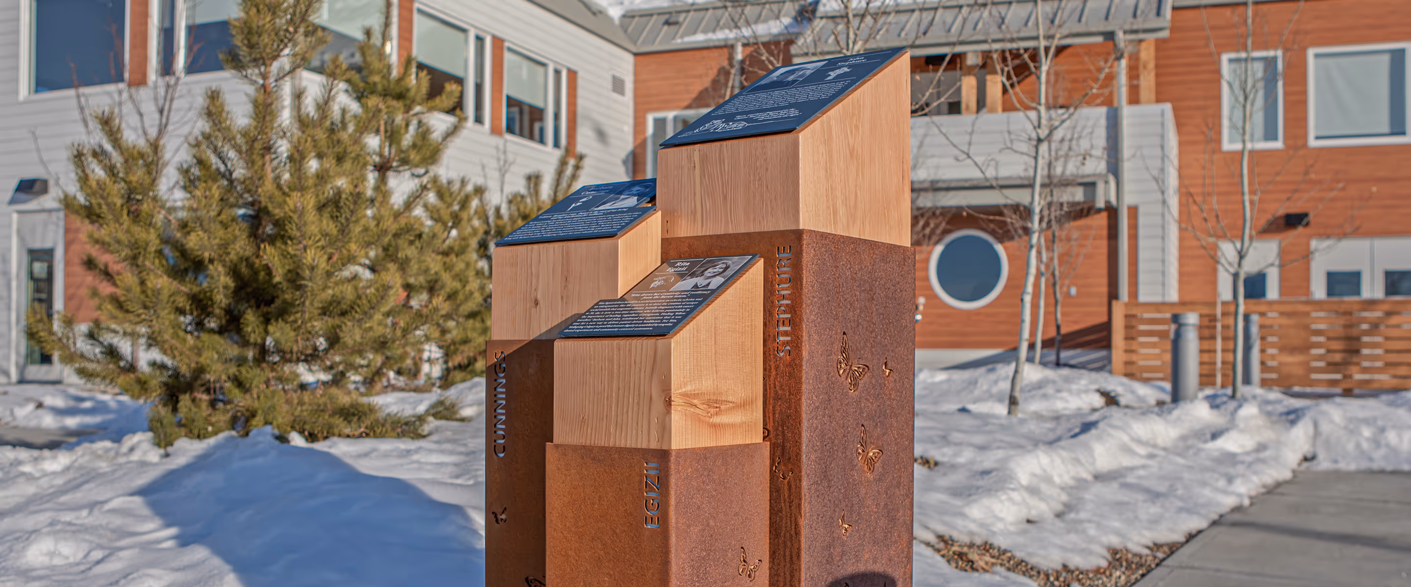 Outdoor donor recognition monument at Wellspring Carma House, featuring wooden pillars wrapped in rusted steel with butterfly cutouts and engraved founder names.