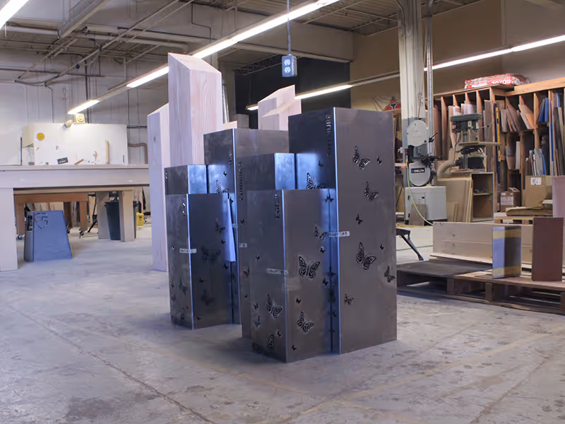 In-progress fabrication of Wellspring donor monument, with steel-encased wooden pillars and butterfly cutouts staged in the workshop.