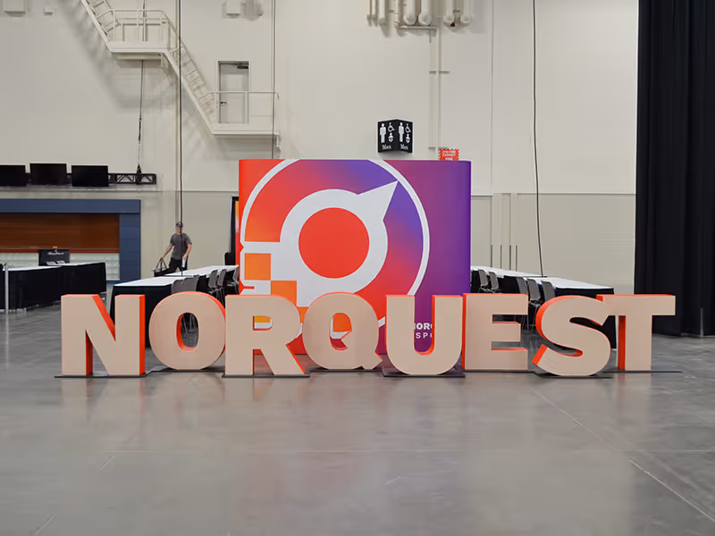 Wide view of a NorQuest College trade show display with large foam letters and a colourful branded pop-up wall.