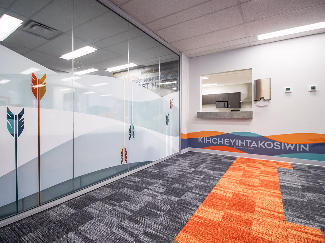 Office interior with decorative privacy film on glass walls, featuring arrow graphics and Indigenous-inspired patterns, with branded wall graphics and carpet accents.