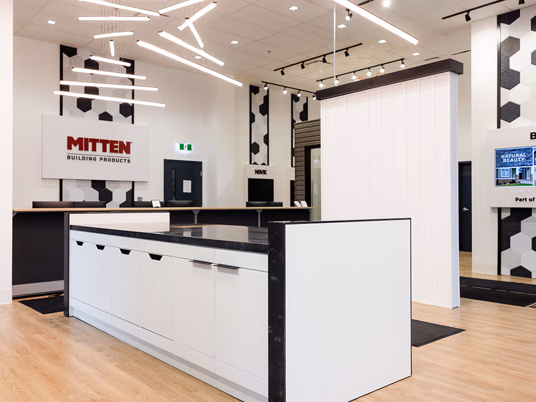 Modern retail sales centre with Mitten Building Products branding, reception counter, display island, feature lighting, and hexagon wall accents.