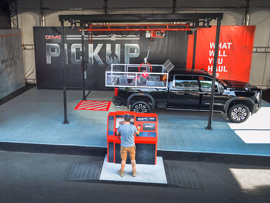 GMC experiential brand activation featuring a pickup truck under a gantry system and interactive console in a large event space.