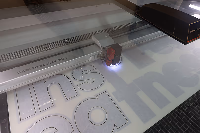 Close-up of Trotec laser machine cutting acrylic lettering for custom trade show display graphics and signage.