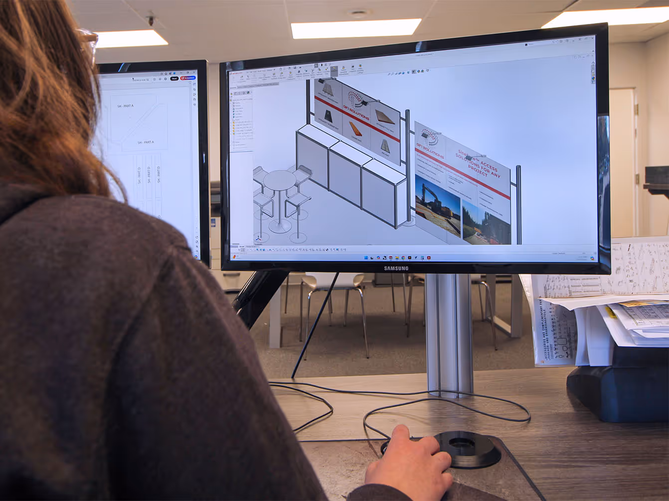 Designer reviewing 3D trade show booth rendering on computer screen during exhibit design development.