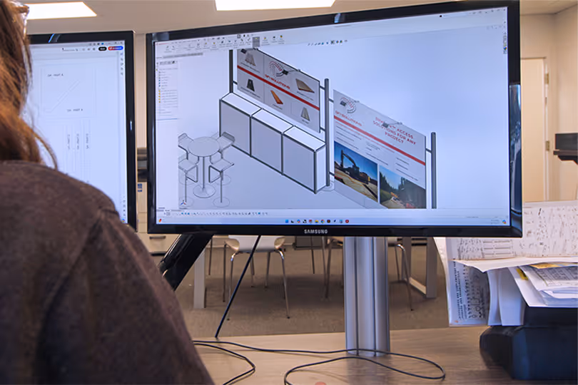 Exhibit designer working on 3D trade show display concept in CAD software, refining booth layout and graphics.