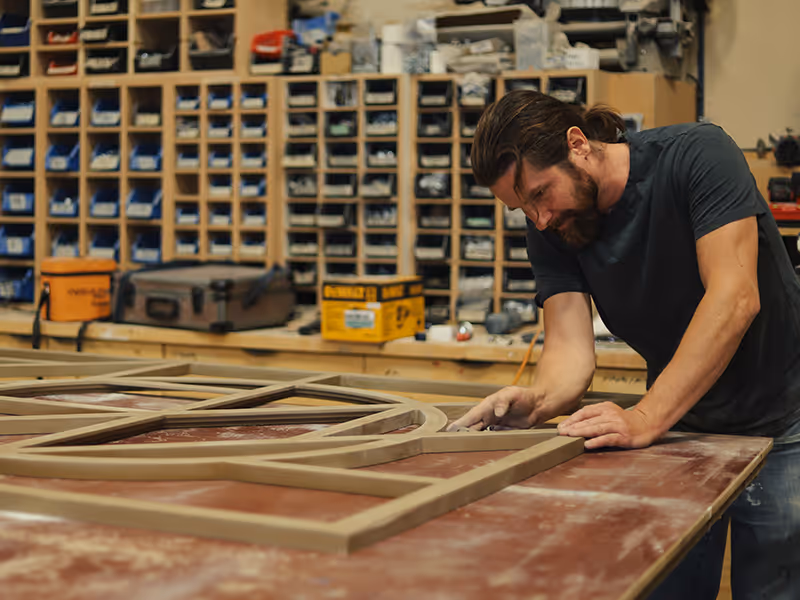 Exhibit Studio fabricator hand-sanding a custom geometric wood frame for the Taza Park marketing centre display in the production workshop.