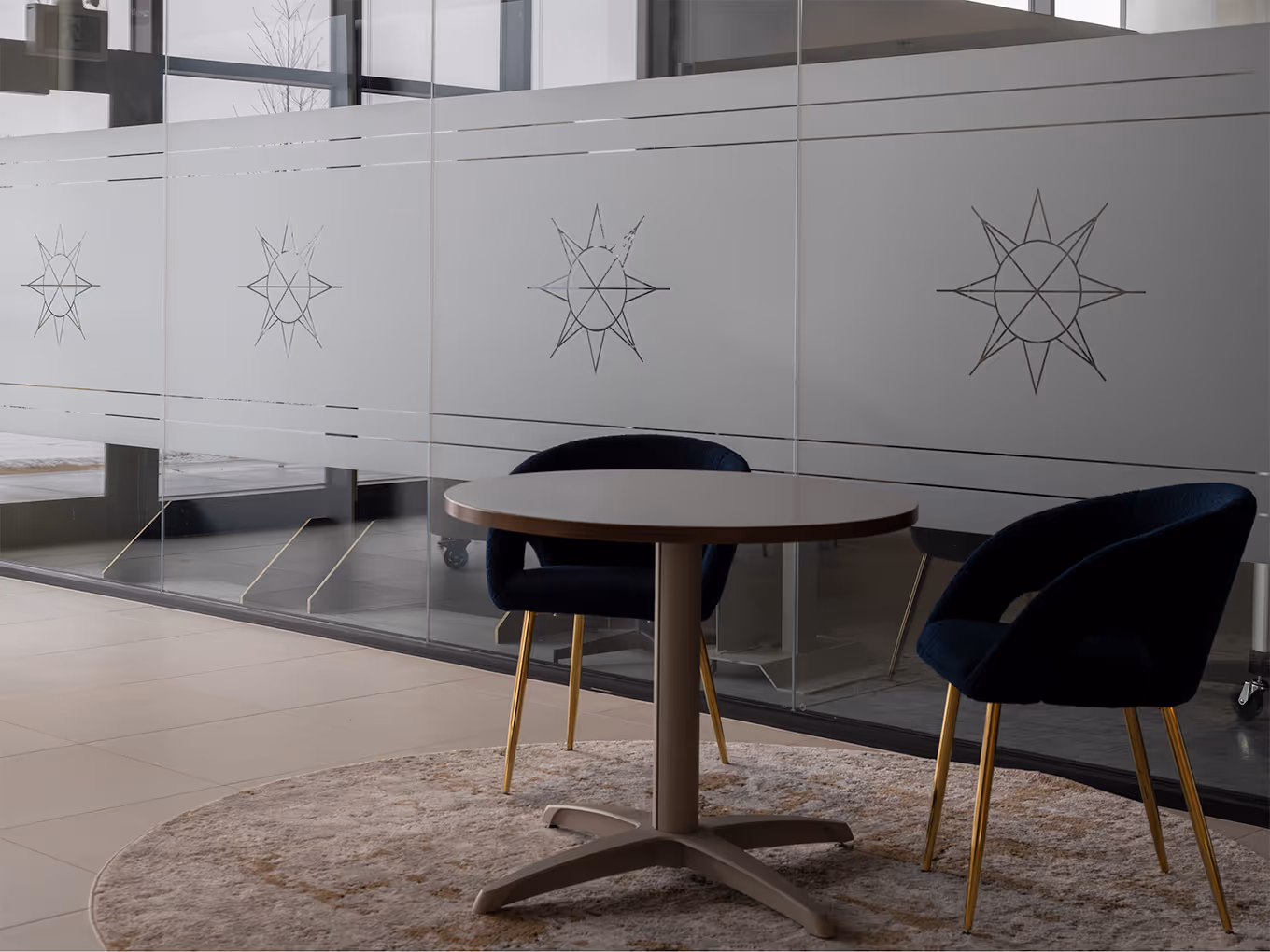 Seating area with round table and navy velvet chairs in front of frosted glass privacy film etched with Taza Park star motifs at the marketing centre.