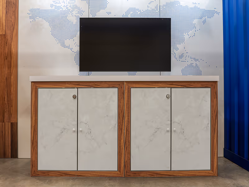 Custom trade show storage cabinets with marble-look panels and wood framing beneath mounted display screen.