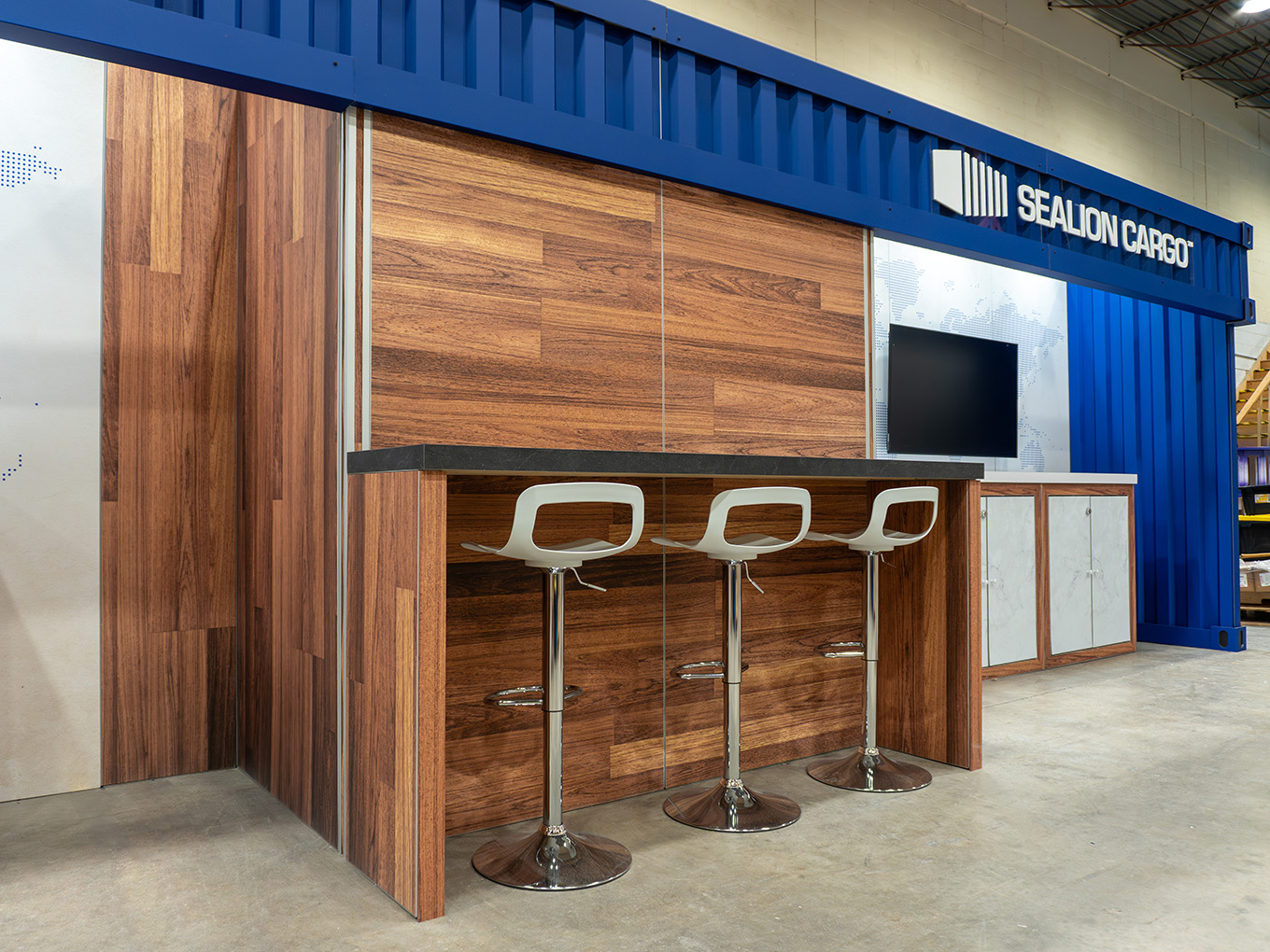 Trade show bar counter with wood finish, high stools, and integrated display within custom shipping container booth.